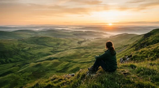 Vista panoramica di colline verdi ondulate all'alba con persona che contempla l'orizzonte